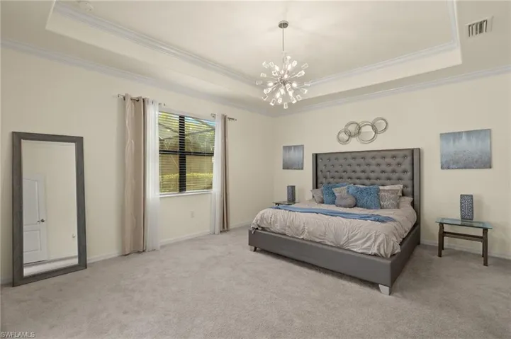 Bedroom with crown molding, a raised ceiling, light colored carpet, and an inviting chandelier