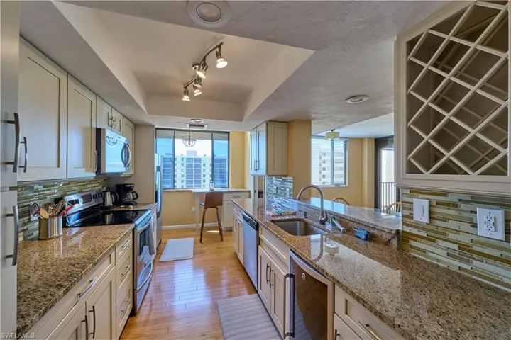 Kitchen featuring backsplash, stainless steel appliances, a raised ceiling, light stone countertops, and light wood finished floors