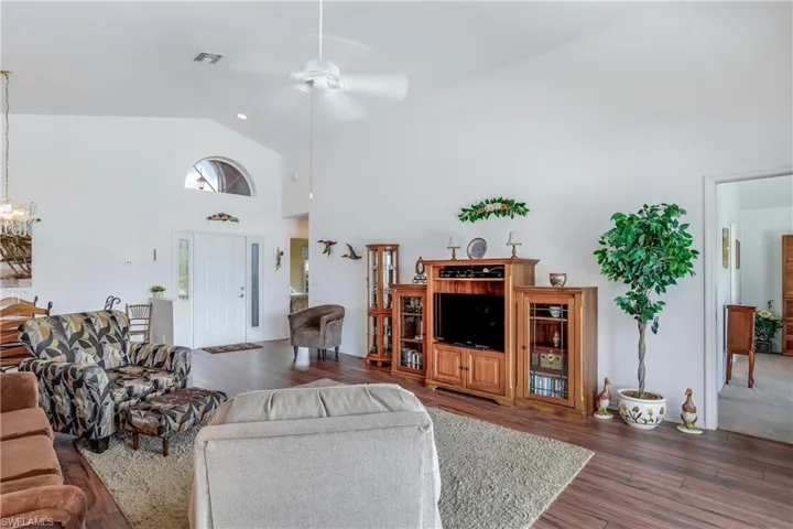 Living room with ceiling fan, dark wood-type flooring, and high vaulted ceiling