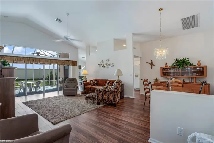 Living room with hardwood / wood-style flooring, ceiling fan with notable chandelier, and high vaulted ceiling