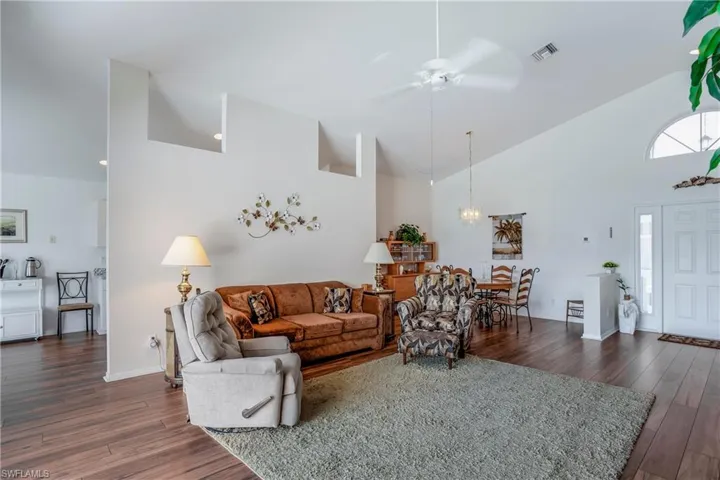 Living room with high vaulted ceiling, ceiling fan, and dark hardwood / wood-style floors
