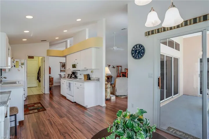 Kitchen with pendant lighting, dark wood-type flooring, white cabinetry, vaulted ceiling, and white appliances