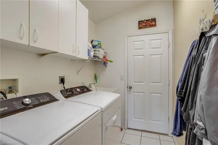 Laundry area with cabinets, light tile patterned floors, separate washer and dryer, and sink