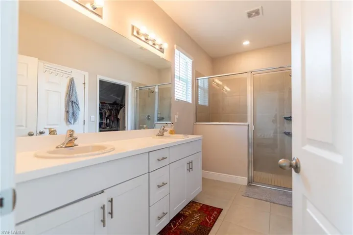 Full bath with double vanity, a shower stall, a walk in closet, and light tile patterned floors