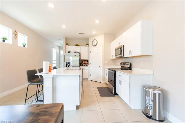Kitchen featuring stainless steel appliances, white cabinets, a breakfast bar, recessed lighting, and a center island with sink