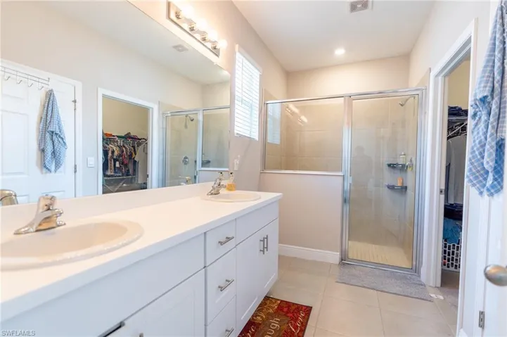 Bathroom featuring a walk in closet, double vanity, light tile patterned floors, and a shower stall