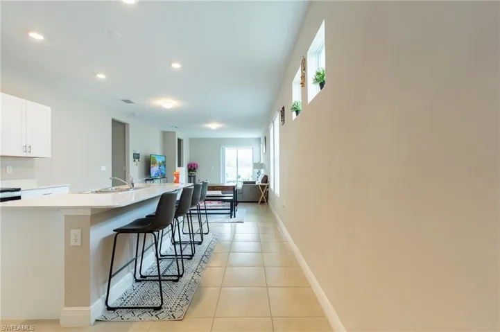 Kitchen with an island with sink, white cabinetry, a breakfast bar area, light tile patterned floors, and light stone counters