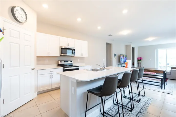Kitchen featuring an island with sink, stainless steel appliances, a kitchen bar, white cabinets, and open floor plan