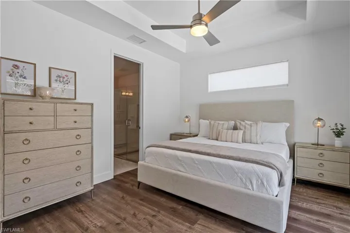 Bedroom with ensuite bathroom, wood finished floors, a ceiling fan, and a tray ceiling