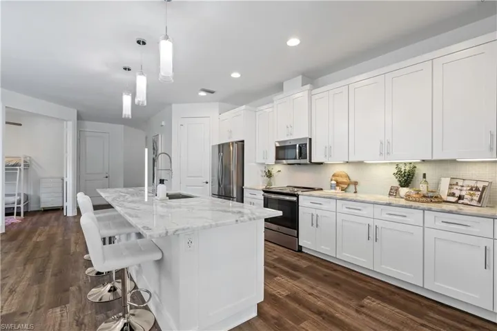 Kitchen with appliances with stainless steel finishes, hanging light fixtures, a center island with sink, white cabinets, and light stone countertops