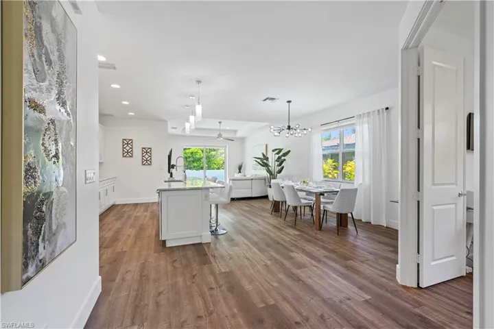 Kitchen featuring a center island with sink, light stone counters, decorative light fixtures, open floor plan, and a kitchen bar