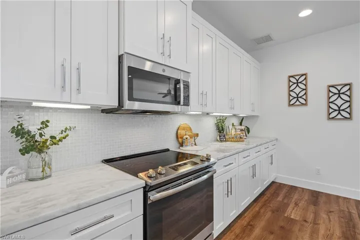 Kitchen featuring stainless steel appliances, white cabinets, light stone counters, and recessed lighting
