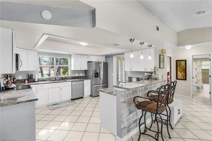 Kitchen featuring white cabinets, stainless steel appliances, light tile patterned floors, a breakfast bar area, and dark stone countertops