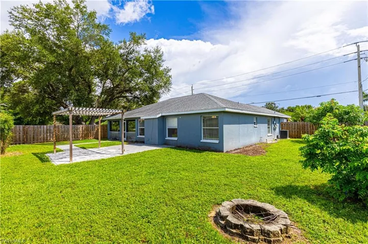 Back of property fenced in with a pergola, spacious lawn, and a patio area, a mango and star fruit tree.