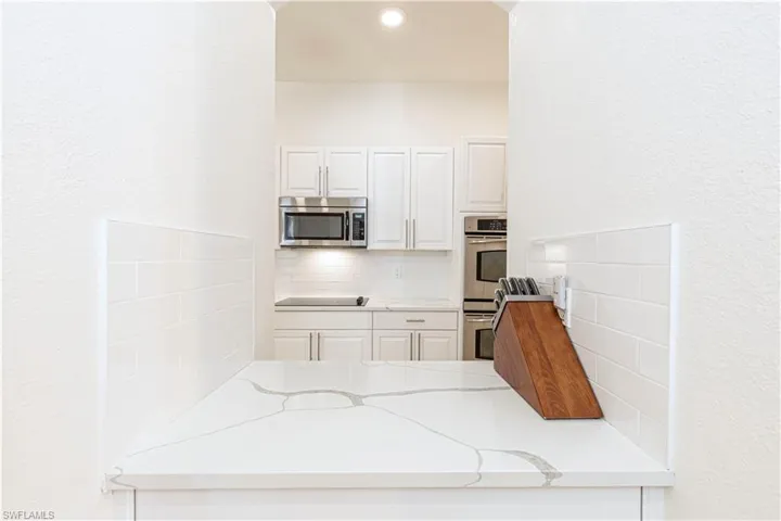 Kitchen featuring white cabinetry, stainless steel appliances, tasteful backsplash, and light stone counters