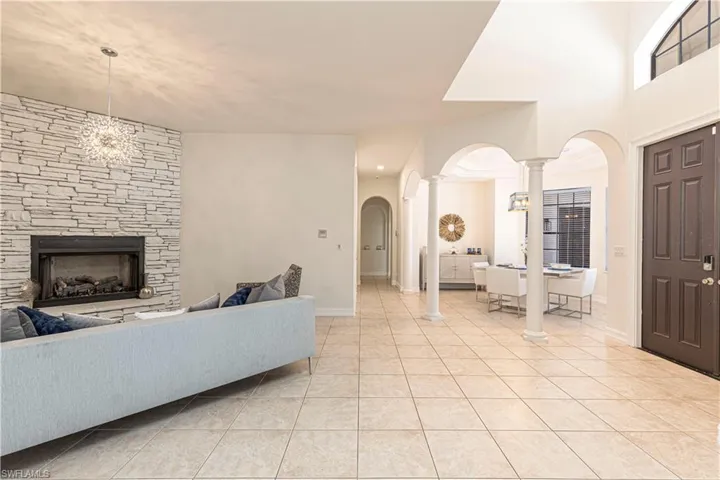 Tiled living room featuring ornate columns, a stone fireplace, and a notable chandelier