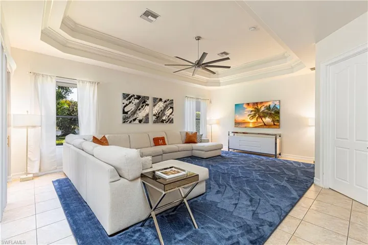 Living room with ceiling fan, light tile patterned floors, and a tray ceiling