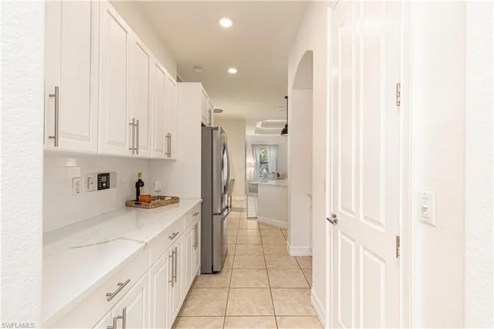 Kitchen with decorative backsplash, light stone counters, white cabinets, light tile patterned floors, and stainless steel fridge