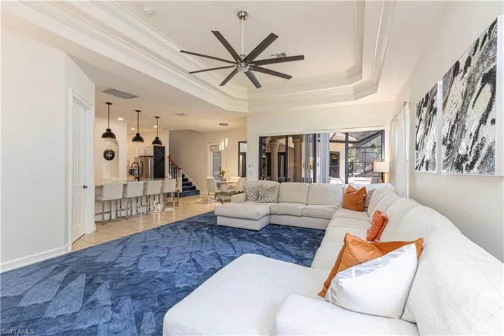 Tiled living room featuring ceiling fan, ornamental molding, and a tray ceiling