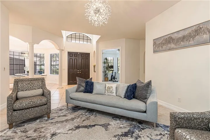 Tiled living room with a wealth of natural light, decorative columns, and a notable chandelier