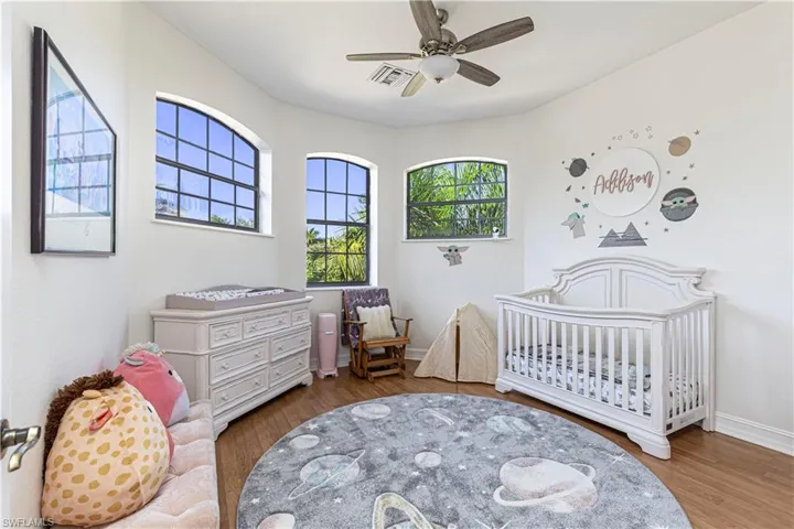 Bedroom featuring ceiling fan, a crib, and wood-type flooring
