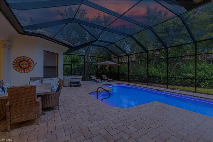 Pool at dusk featuring glass enclosure and a patio area