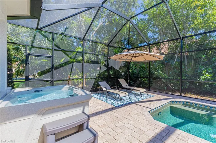 View of pool with a hot tub, glass enclosure, and a patio