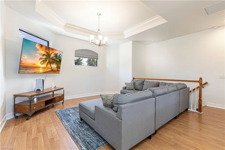 Living room with light wood-type flooring, a raised ceiling, crown molding, and a chandelier