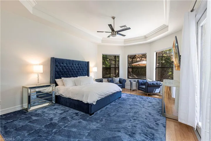 Bedroom featuring ceiling fan, ornamental molding, a tray ceiling, and wood-type flooring
