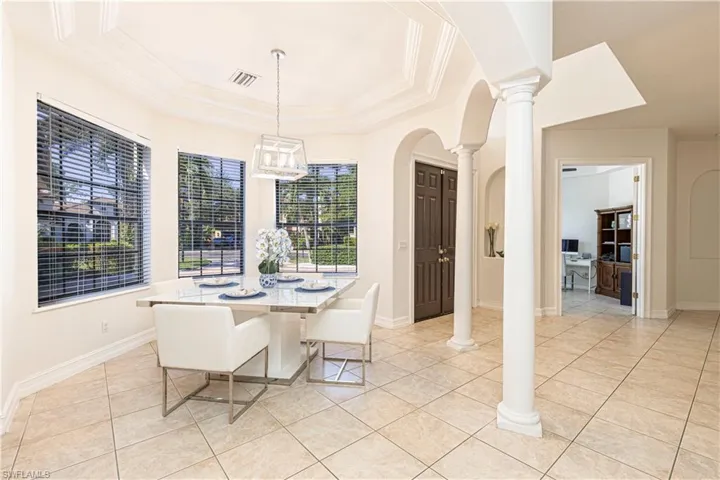 Tiled dining area featuring decorative columns and a tray ceiling