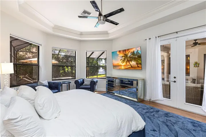 Bedroom with ornamental molding, french doors, wood-type flooring, a tray ceiling, and ceiling fan