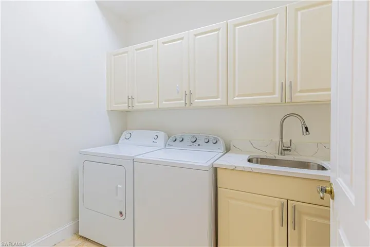 Laundry room with sink, washing machine and dryer, light tile patterned floors, and cabinets