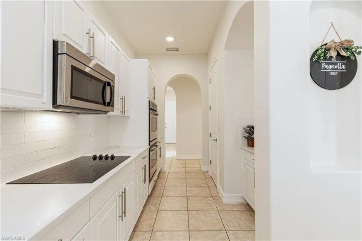 Kitchen featuring backsplash, stainless steel appliances, light stone countertops, white cabinets, and light tile patterned floors