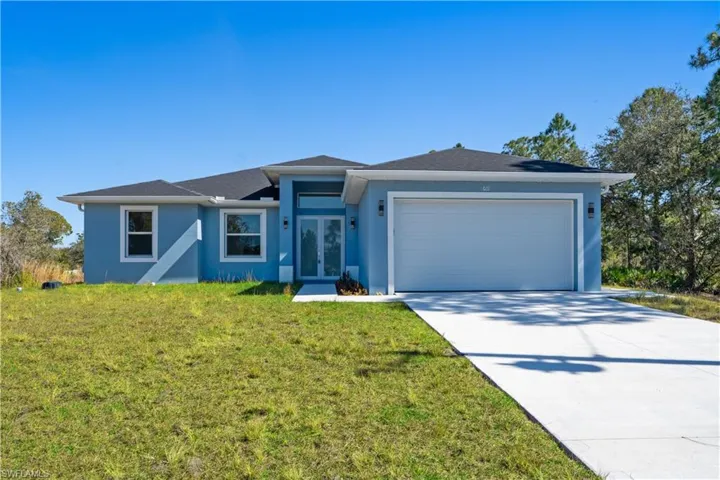 View of front of home with an attached garage, concrete driveway, a front lawn, and stucco siding