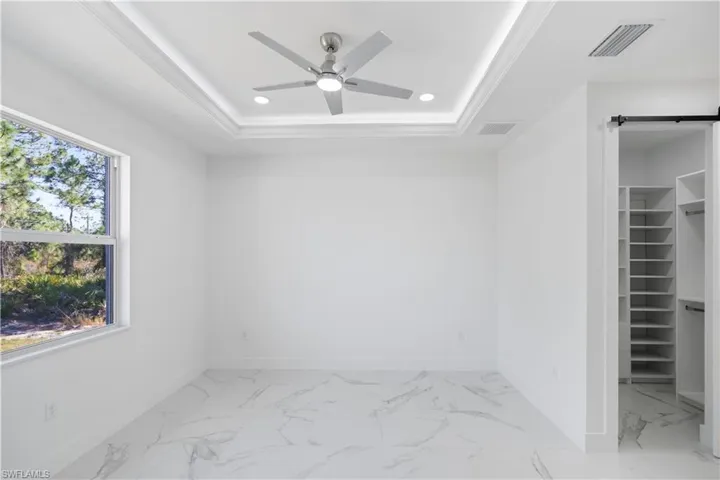 Unfurnished bedroom featuring a walk in closet, recessed lighting, a barn door, light marble finish floors, and a raised ceiling