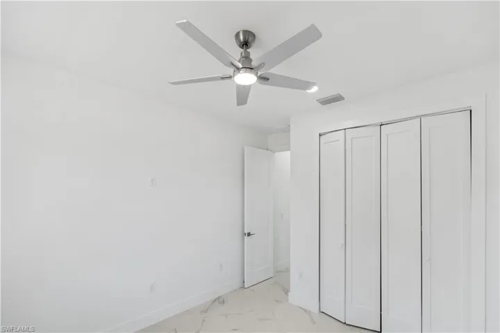 Unfurnished bedroom featuring light marble finish floors, a closet, and a ceiling fan