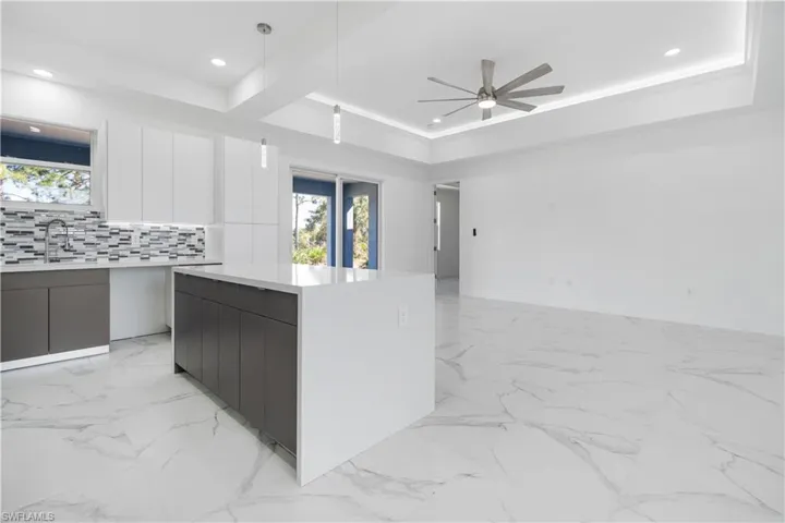 Kitchen with modern cabinets, two tone color scheme, decorative backsplash, light stone countertops, and ceiling fan