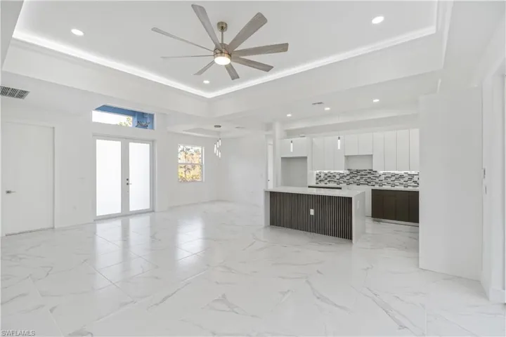 Unfurnished living room featuring ceiling fan, recessed lighting, french doors, a raised ceiling, and light marble finish flooring