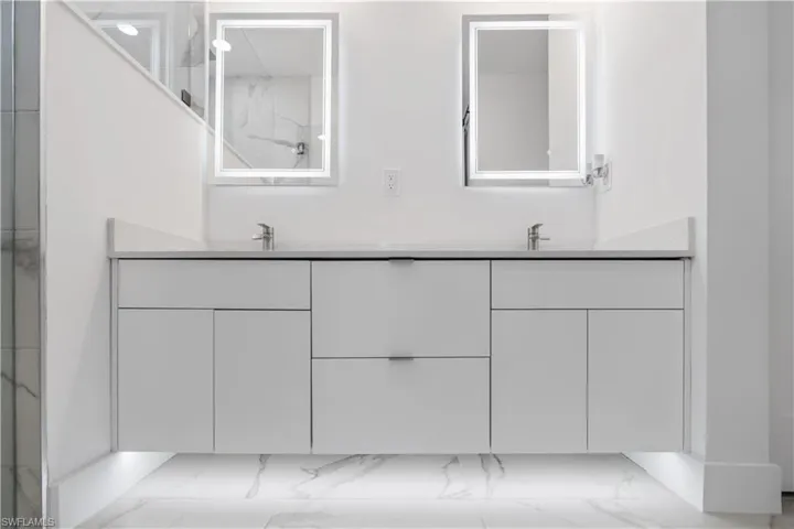 Full bath featuring double vanity, light marble finish floors, and a shower