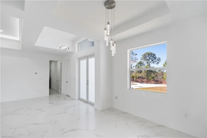 Unfurnished dining area featuring french doors, light marble finish floors, and a tray ceiling