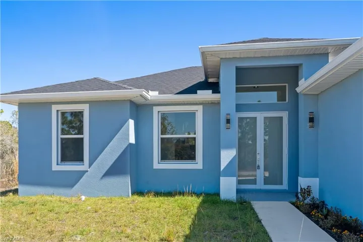Doorway to property featuring french doors, stucco siding, a lawn, and a shingled roof