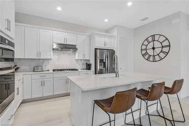 Kitchen with a breakfast bar area, stainless steel appliances, light countertops, under cabinet range hood, and backsplash