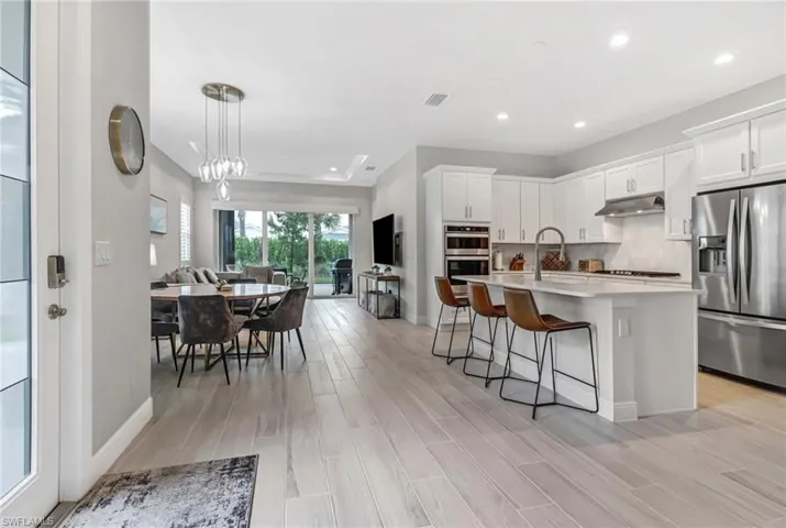 Kitchen featuring wood tiled floor, a breakfast bar, under cabinet range hood, appliances with stainless steel finishes, and backsplash