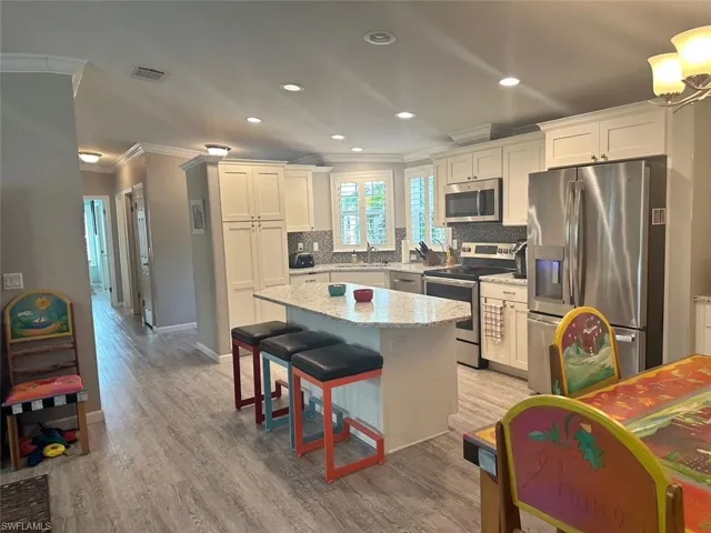Kitchen featuring appliances with stainless steel finishes, white cabinetry, sink, a center island, and light wood-type flooring