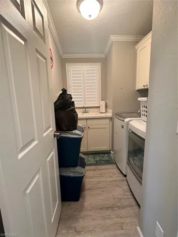 Laundry room featuring sink, washer and clothes dryer, cabinets, light hardwood / wood-style floors, and a textured ceiling