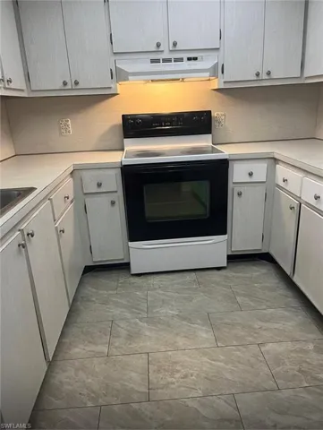 Kitchen with electric stove, under cabinet range hood, and light countertops