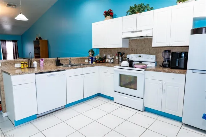 Kitchen featuring white appliances, backsplash, decorative light fixtures, under cabinet range hood, and white cabinetry