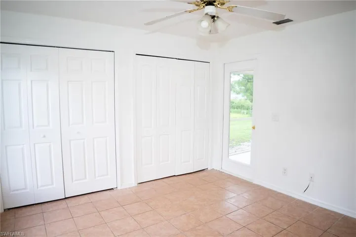 Unfurnished bedroom with two closets, light tile patterned flooring, a ceiling fan, and access to exterior