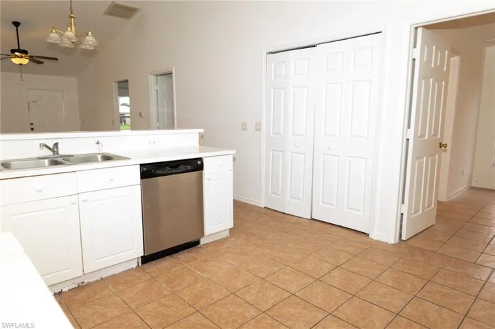 Kitchen with white cabinetry, stainless steel dishwasher, light countertops, light tile patterned floors, and vaulted ceiling
