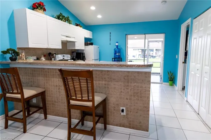 Kitchen featuring a peninsula, a breakfast bar, white cabinets, light tile patterned floors, and backsplash